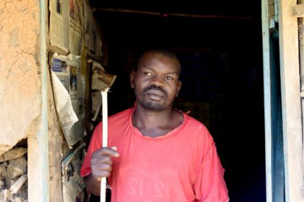 Ein afrikanischer Mann mit Stock im Eingang einer Hütte, in der es dunkel ist.