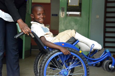 Ein lachender Junge mit Gipsbeinen sitzt im Rollstuhl.