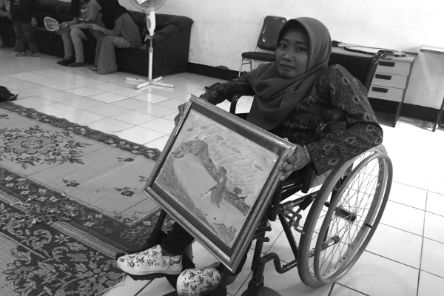 Eine Frau im Rollstuhl hält ein gerahmtes Landschaftsbild.