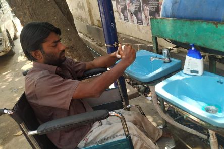 Ein Mann im Rollstuhl wäscht sich die Händer in einem Keramikwaschbecken im Freien