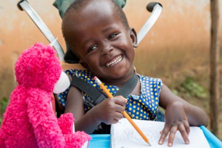 Die sechsjährige Justine aus Uganda wurde mit Hydrozephalus (&quot;Wasserkopf&quot;) geboren. Ein CBM-Gemeindehelfer fand die Sechsjährige: Jetzt bekommt sie regelmäßig Physiotherapie und macht tolle Fortschritte. Auf dem Bild freut sie sich über ein Geschenk - einen rosa Teddybären.