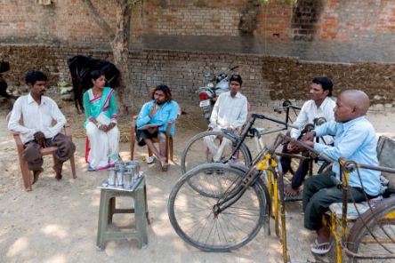 Männer und Frauen, zwei mit Tricyle, sitzen im Kreis.