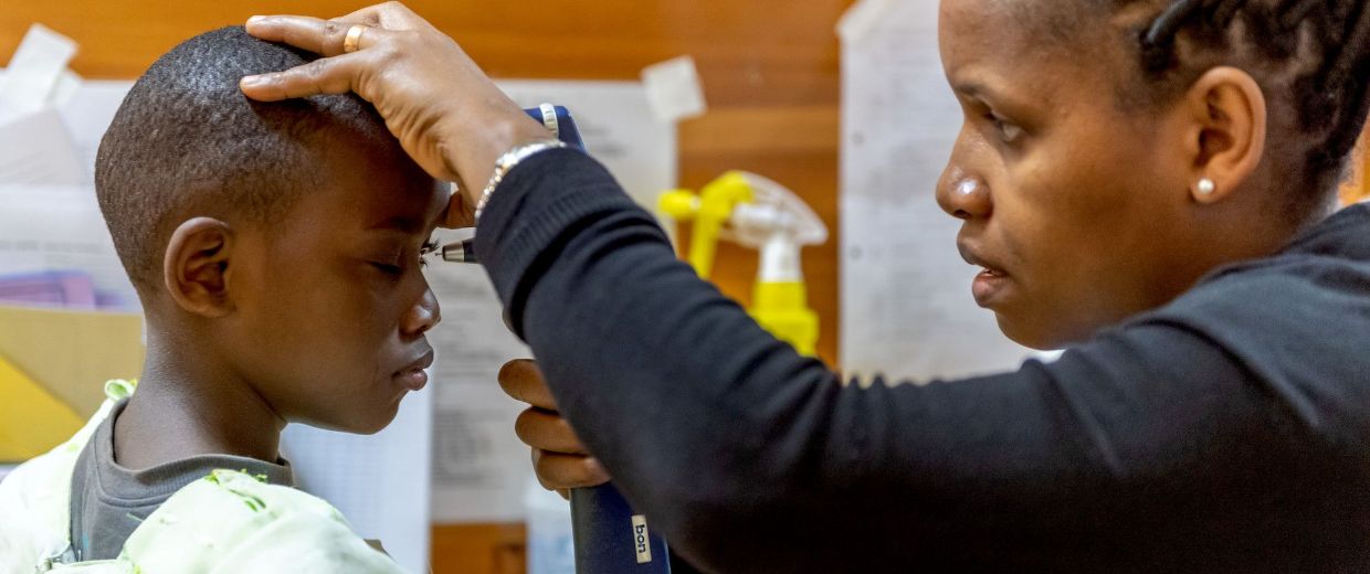 Eine Frau hält ein Untersuchungsgerät vor das Auge eines Kindes