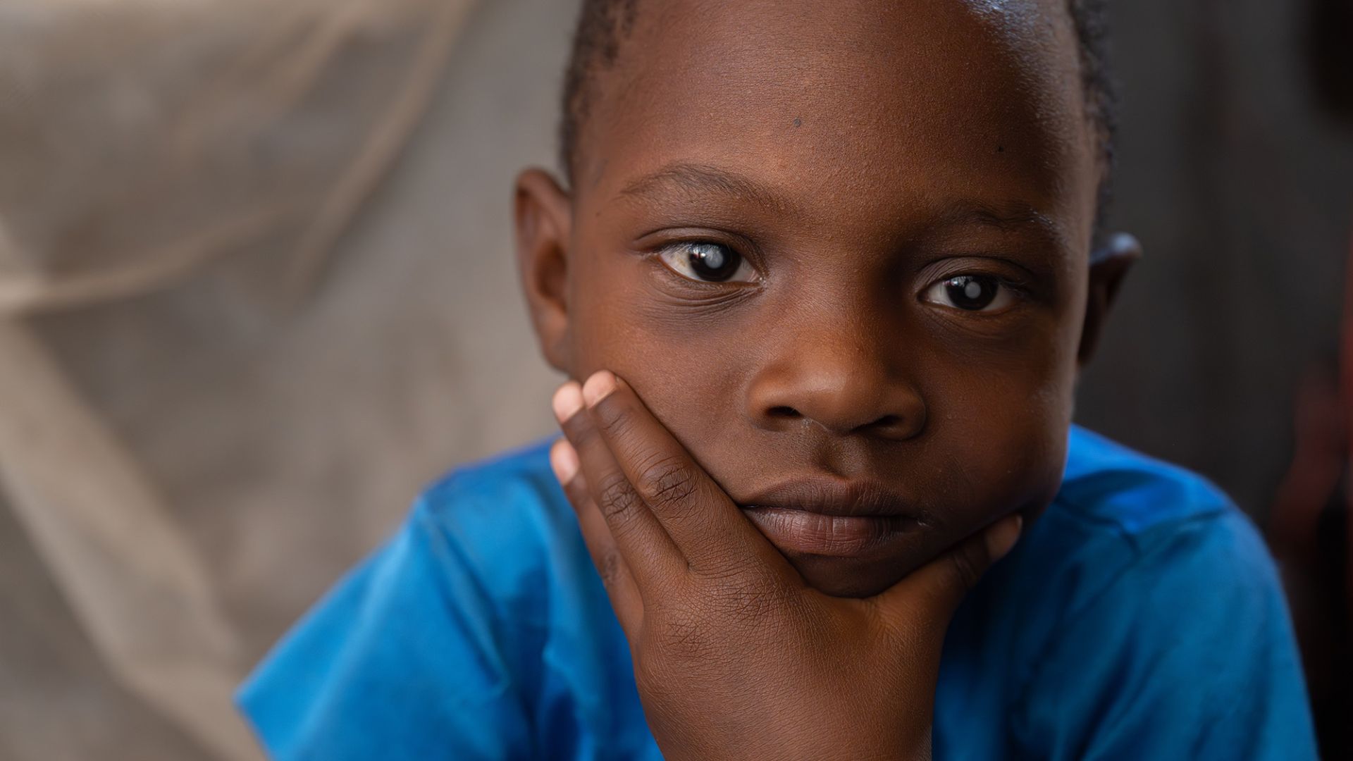 Ein etwa fünfjähriges Mädchen mit weißen Pupillen hat das Kinn auf die Hand gestützt.