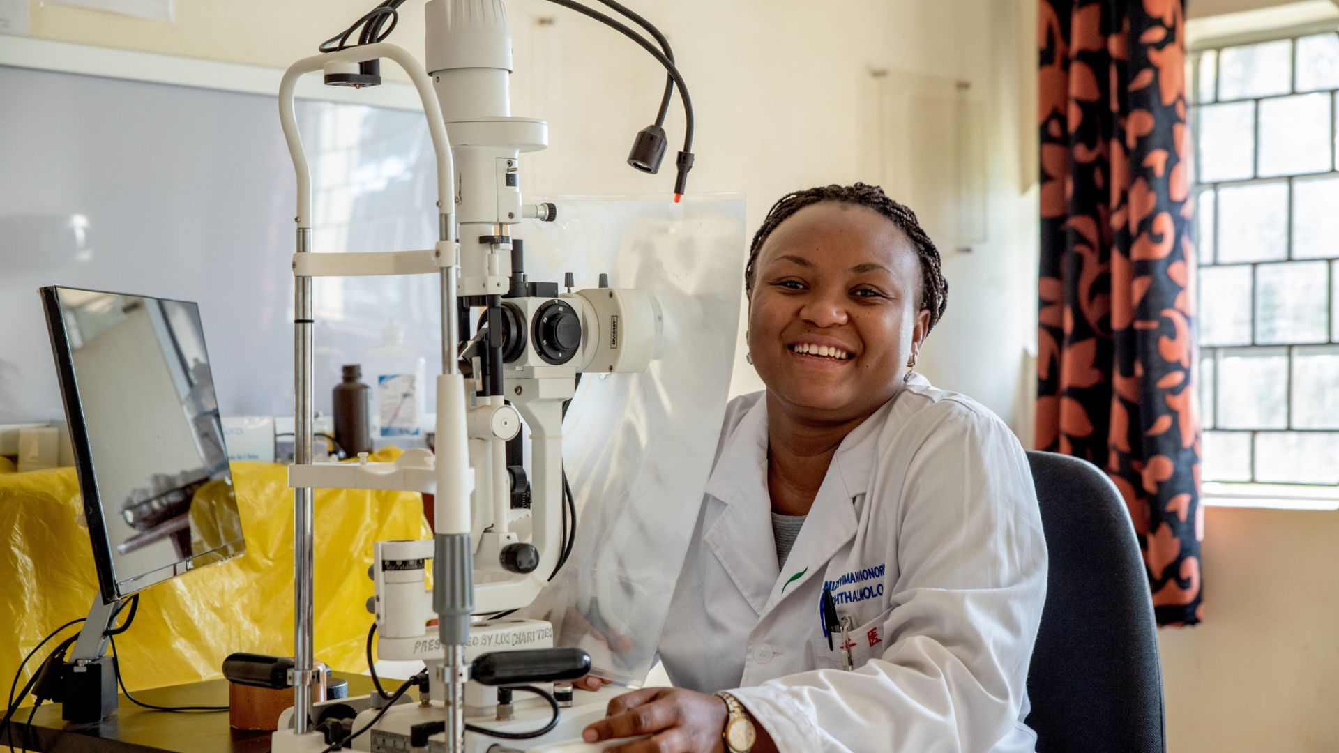 Afrikanische Frau im weißen Kittel sitzt an einem Apparat zur Untersuchung von Augen
