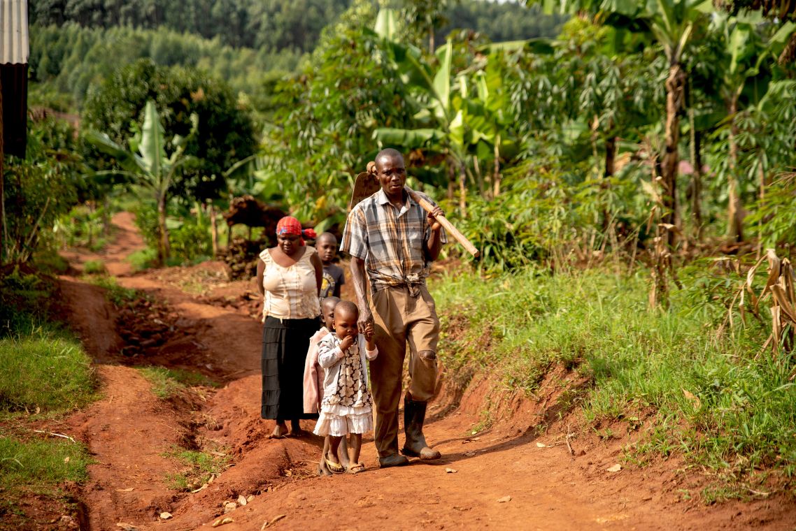 Ein Mann mit Hacke über der Schulter geht mit einem kleinen Mädchen an der Hand einen Feldweg entlang. Eine Frau folgt ihnen.