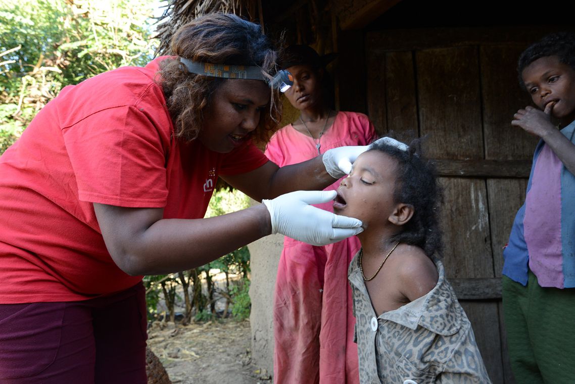 Momina wird von einer CBM Mitarbeiterin am Auge behandelt. Sie steht im Hintergrund sieht man ihre Mutter.