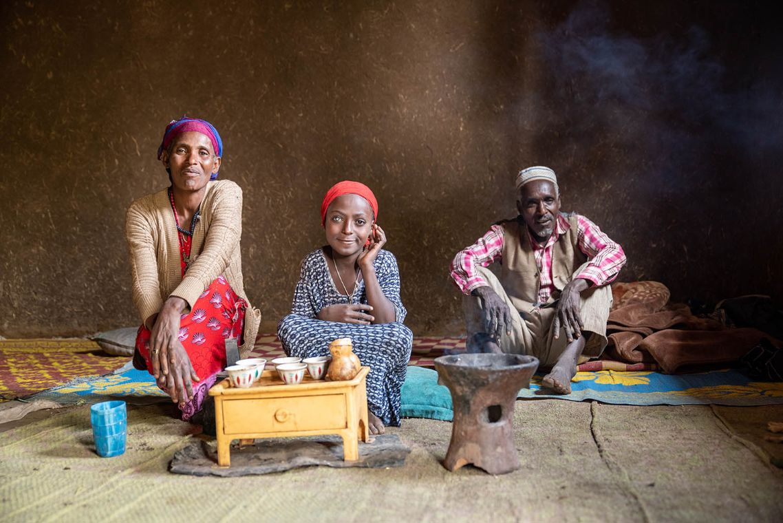 Mulunesh sitzt mit ihren Eltern ihrer Hütte auf dem Boden. Vor ihnen steht ein kleiner Tisch mit Tassen.