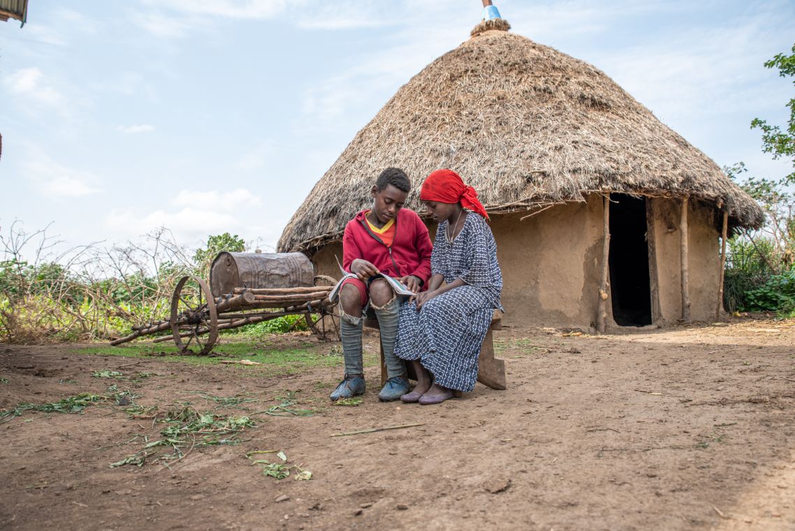 Mulunesh und ihr Bruder sitzen vor der Hütte und schauen zusammen in ein Buch.