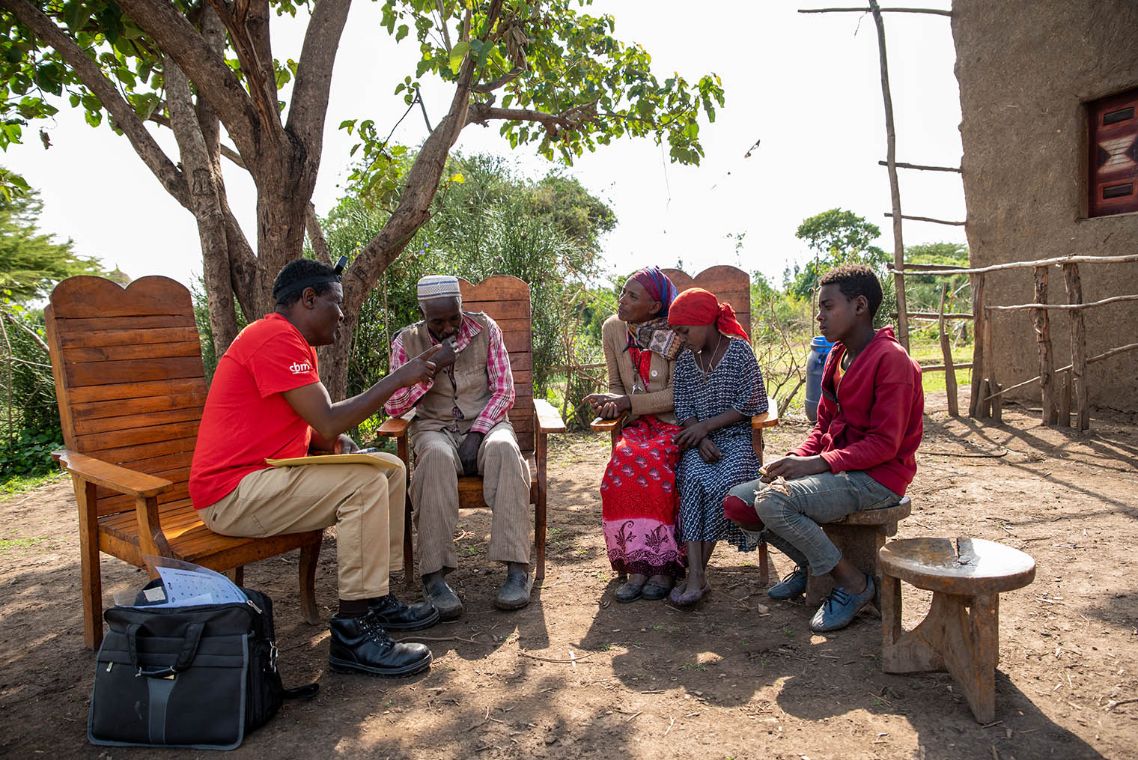 Auf dem Bild sitzt Mulunesh mit ihrer Familie mit einem Arbeiter der CBM in einem Kreis. Sie hören ihm zu.