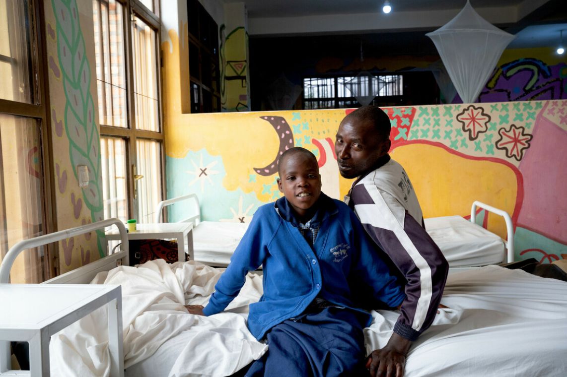 Ein Mädchen und ein Mann sitzen auf einem Krankenbett und lachen.