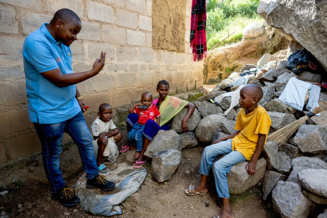 Ein etwa zehnjähriger Junge sitzt auf einem Steinbrocken, vor ihm steht ein Mann im CBM-T-Shirt und streckt zwei Finger der rechten Hand hoch.