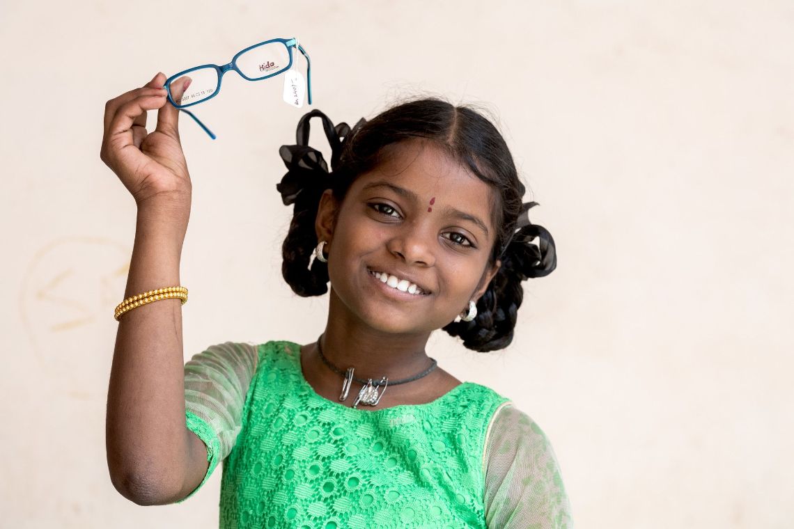 Ein Mädchen hält lachend eine Brille hoch.