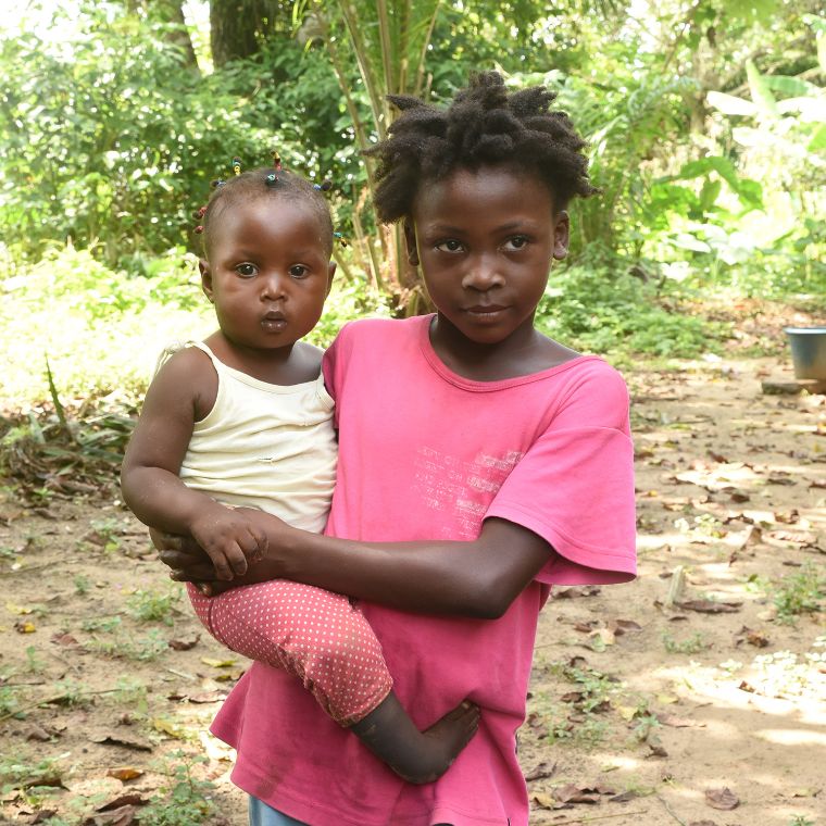 Ein Kleinkind steht vor einem Plastikstuhl, an dem es sich festhält.