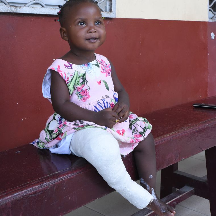 Zwei Männer in weißen Kitteln gipsen das Bein eines kleinen Mädchens ein, eine Frau steht dabei.