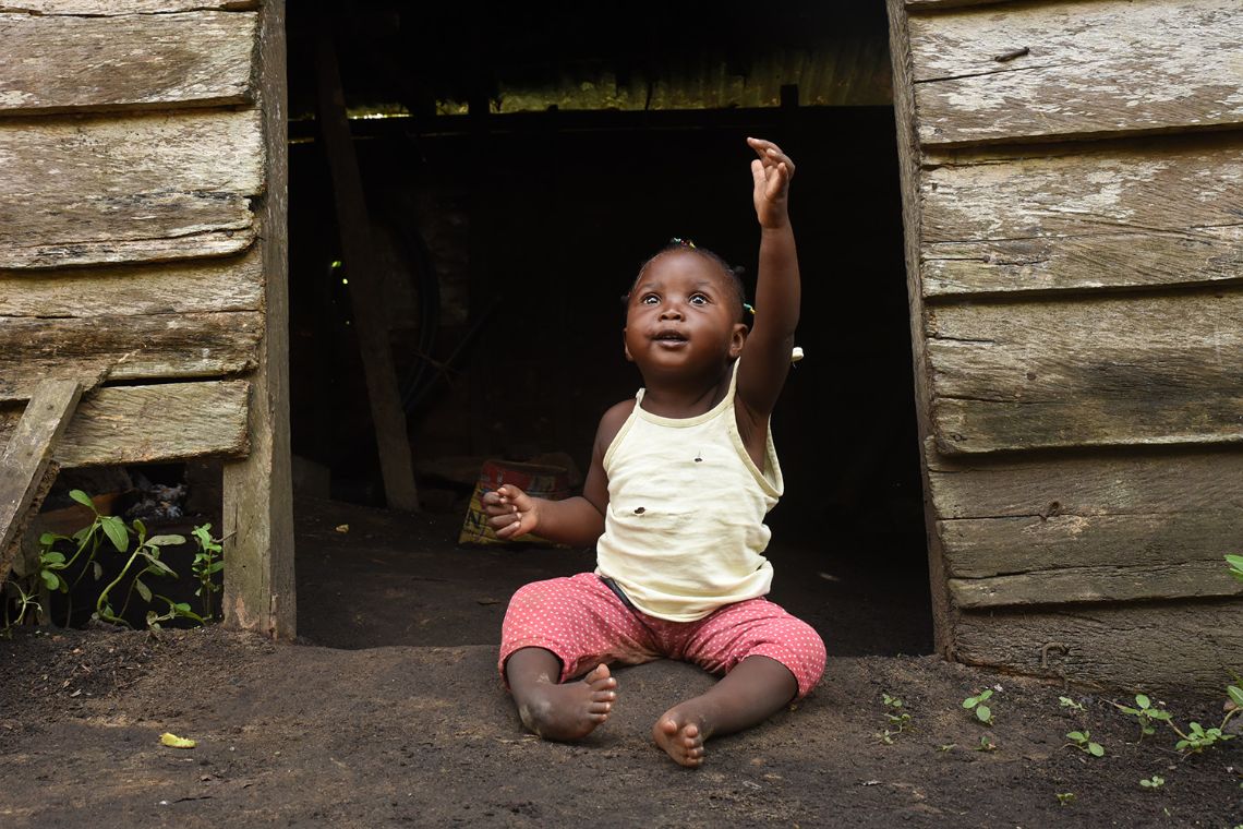 Kleines winkendes Mädchen, das im Eingang zu einer Hütte sitzt
