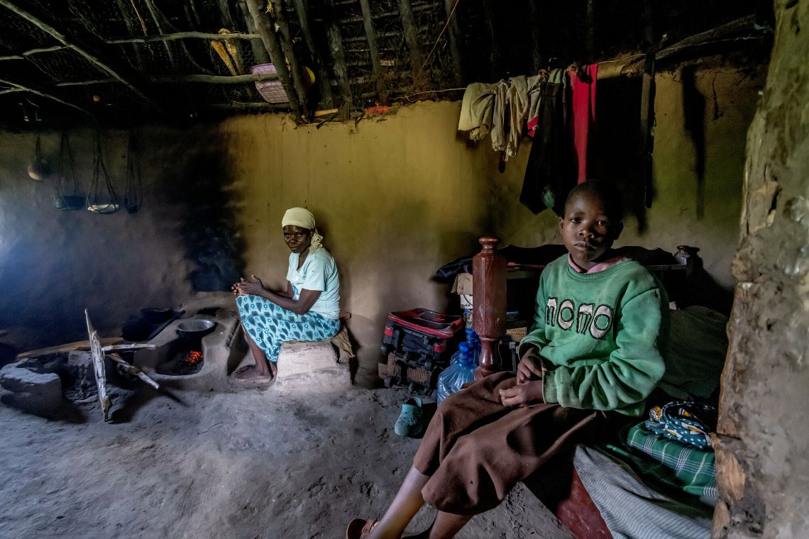 Ein Mädchen und einer Frau im Inneren einer Hütte, in dem ein Kochfeuer brennt.