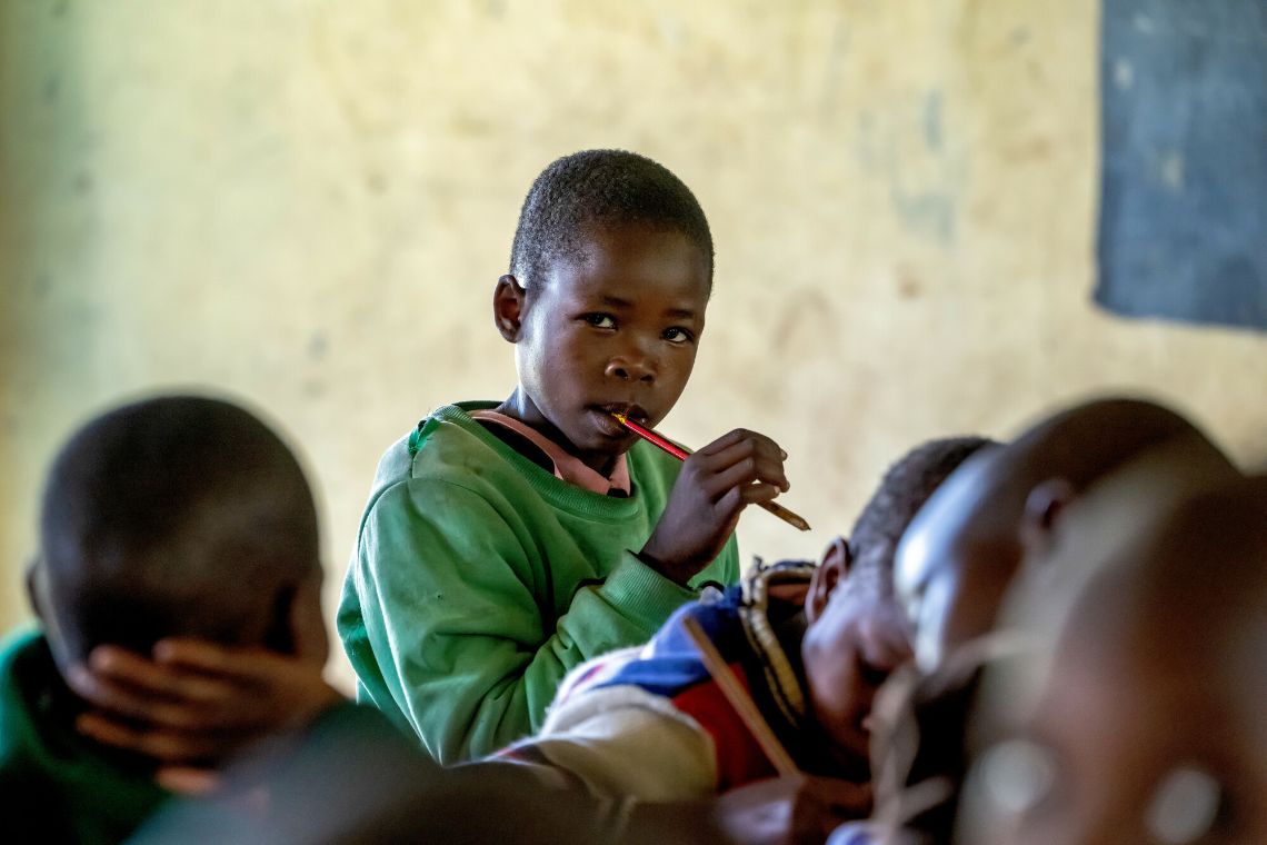 Ein Mädchen, das einen Stift in der Hand hält, inmitten anderer Kinder in einem Klassenzimmer