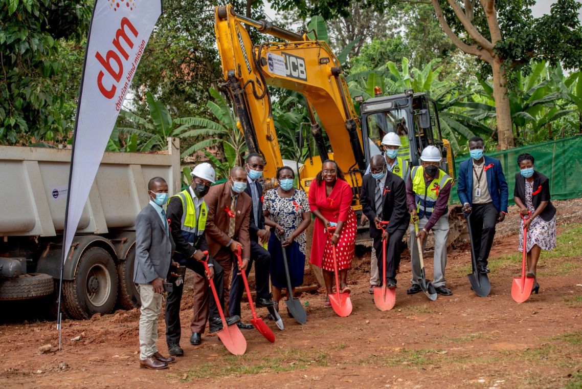 Zehn Menschen mit roten Handschaufeln, im Hintergrund ein LKW und ein Bagger