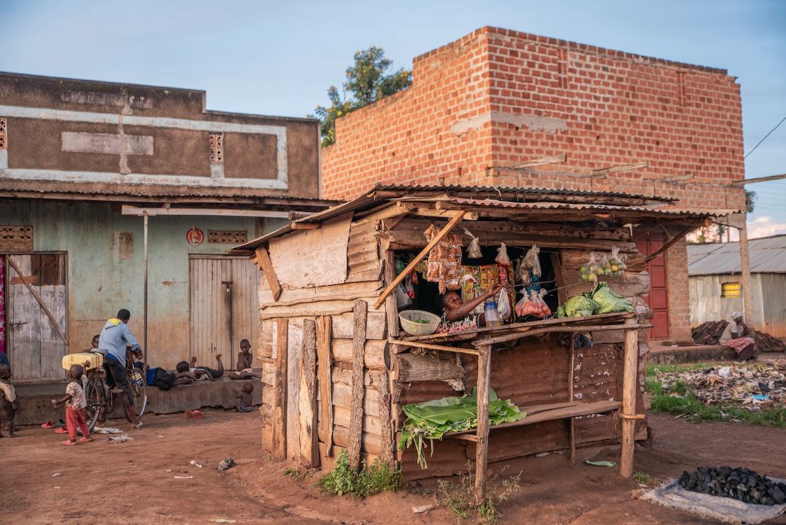 Vor anderen Gebäuden steht eine kleine Holzhütte mit einer geöffneten Klappe, auf der Waren ausgelegt sind.