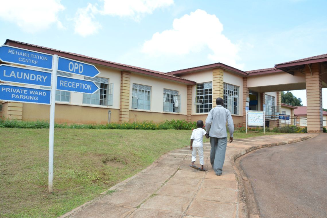 Ein Mann geht mit einem kleinen Jungen an der Hand auf den Eingang eines Gebäudes zu.
