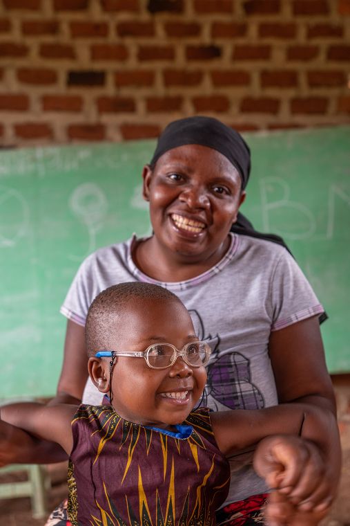 Kleines Mädchen mit Brille lehnt sich an eine lachende Frau