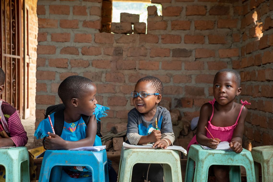 Drei kleine Mädchen schreiben in Hefte, die auf kleinen, bunten Plastikhockern liegen.