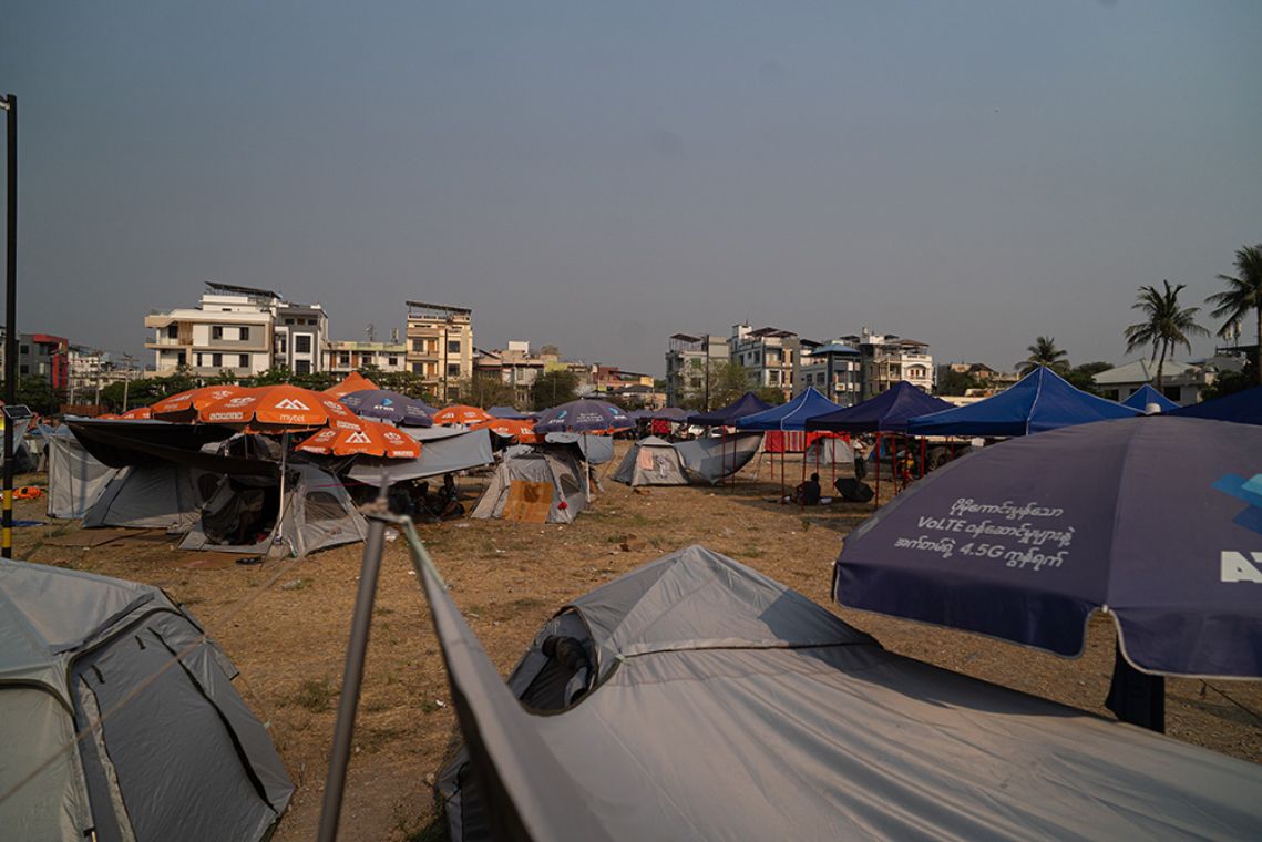 Zelte und Sonnenschirme auf einem Platz vor mehrgeschossigen Gebäuden.