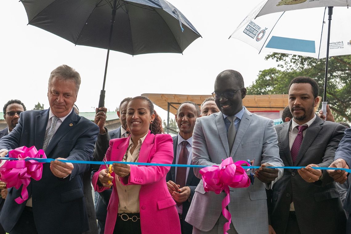 Eine Frau im Blazer und drei Männer im Anzug halten ein vor ihnen gespanntes Band, das mit zwei rosa Schleifen geschmückt ist. Die Frau und ein Mann halten jeweils eine Schere ans Band.