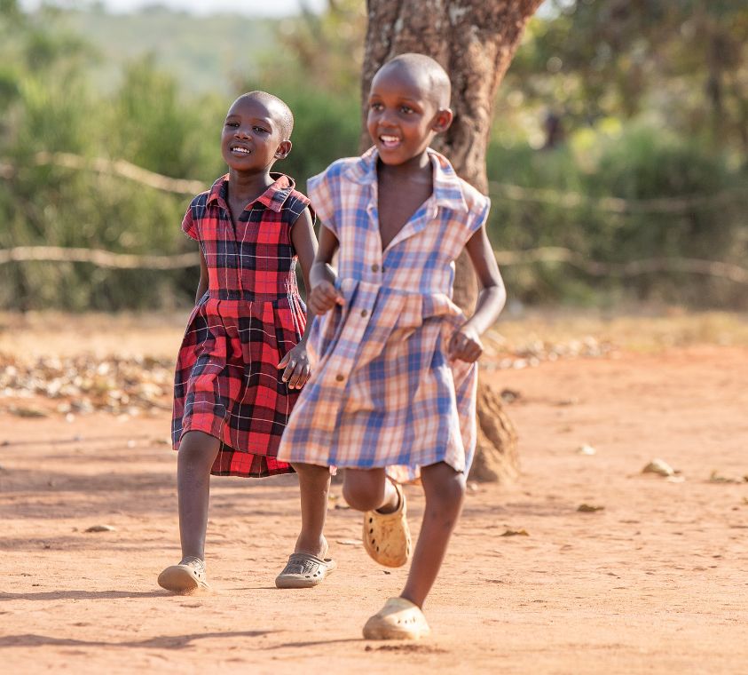 Zwei kleine Mädchen in karierten Kleidchen rennen über einen sandigen Platz.