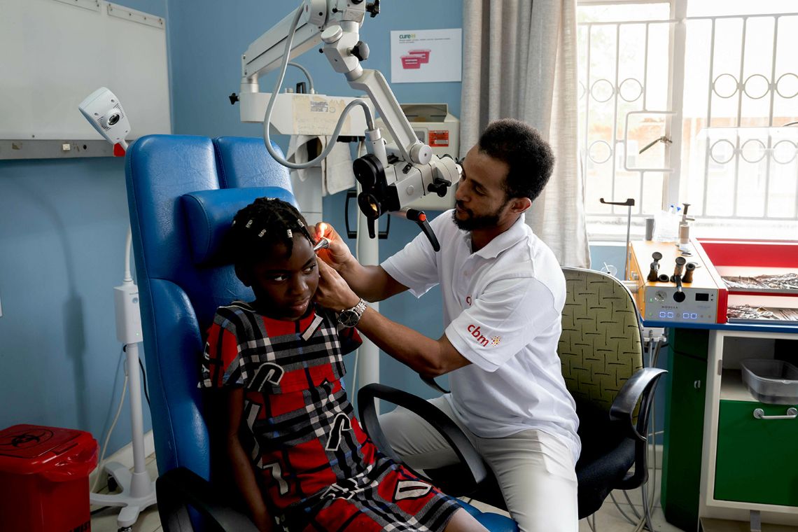 Ein Mann mit weißem CBM-Shirt untersucht die Ohren eines etwa zehnjährigen Mädchens.