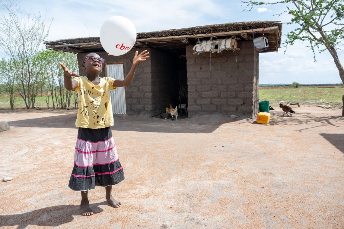 Ein etwa achtjähriges Mädchen mit Brille wirft einen Luftballon in die Luft.