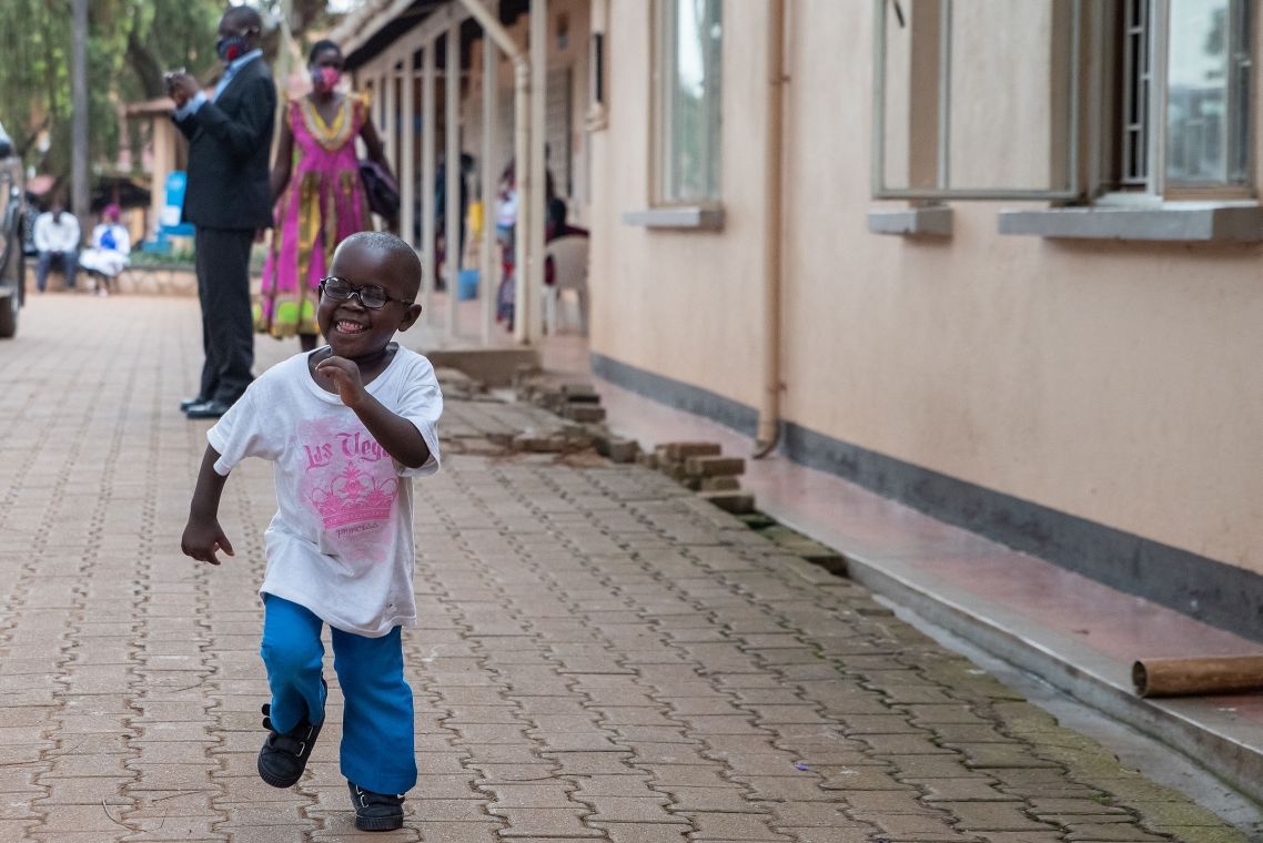 Kleiner Junge rennt lächelnd auf einem gepflasterten Weg entlang.