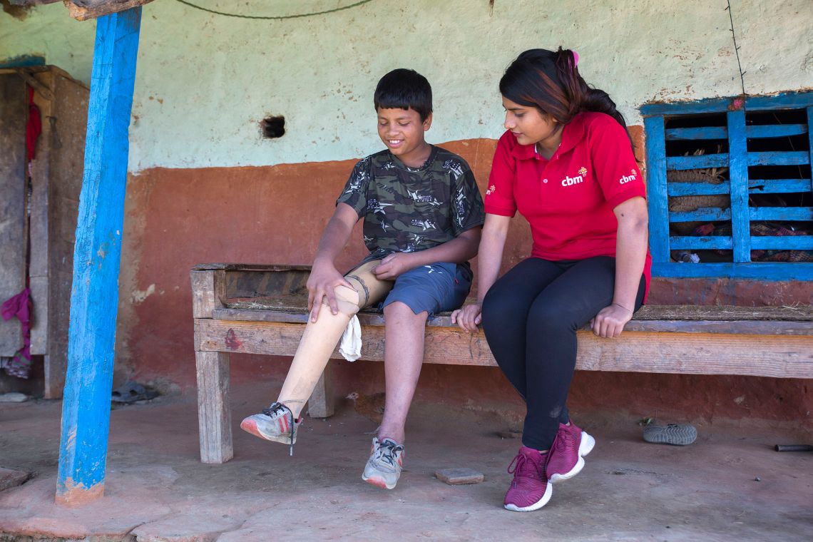 Junge mit Beinprothese und eine Frau sitzen zusammen auf einer Bank.