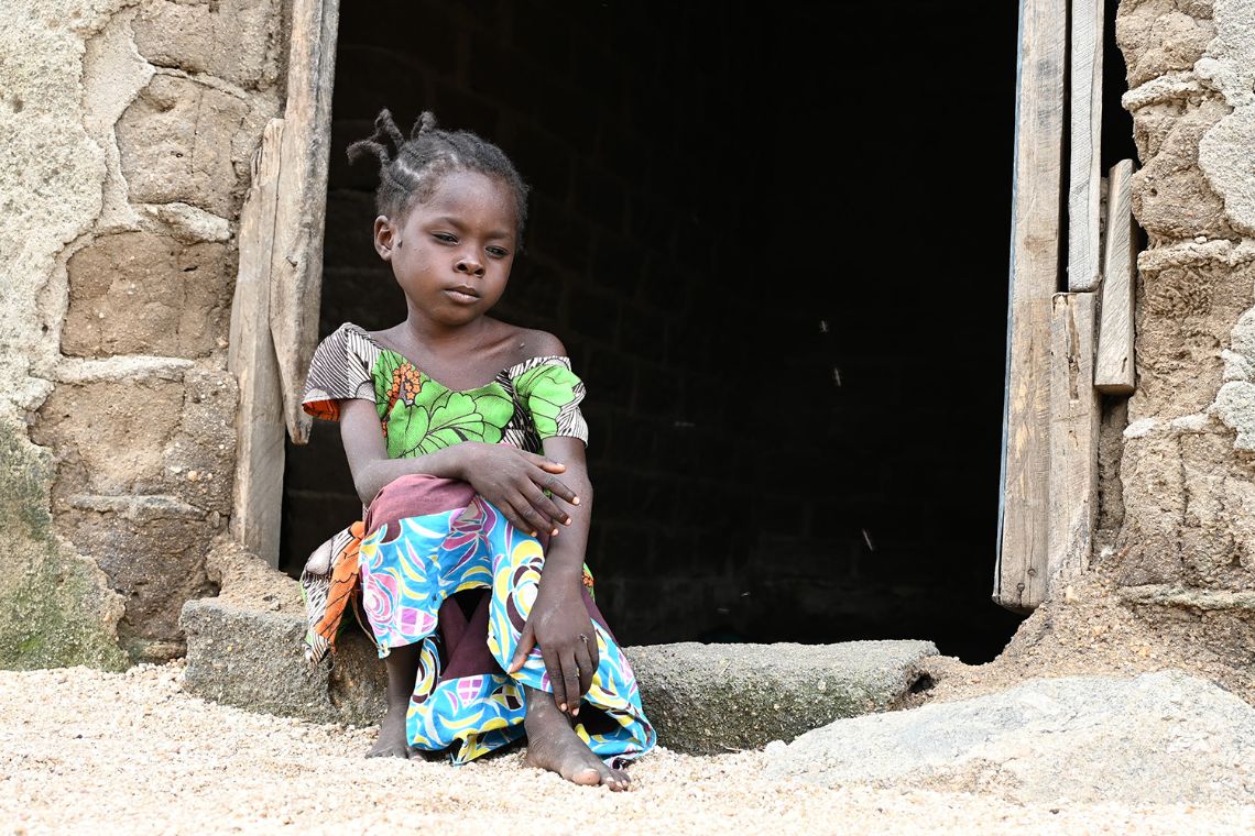 Ein etwa achtjähriges Mädchen sitzt im Türrahmen einer gemauerten Hütte.