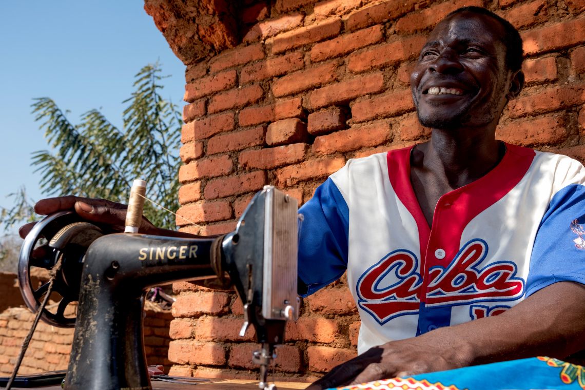 Ein afrikanischer Mann sitzt im Freien an einer Nähmaschine. 