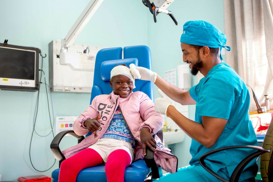 Ein Mann in OP-Kleidung legt einem Mädchen einen Ohrenverband an.