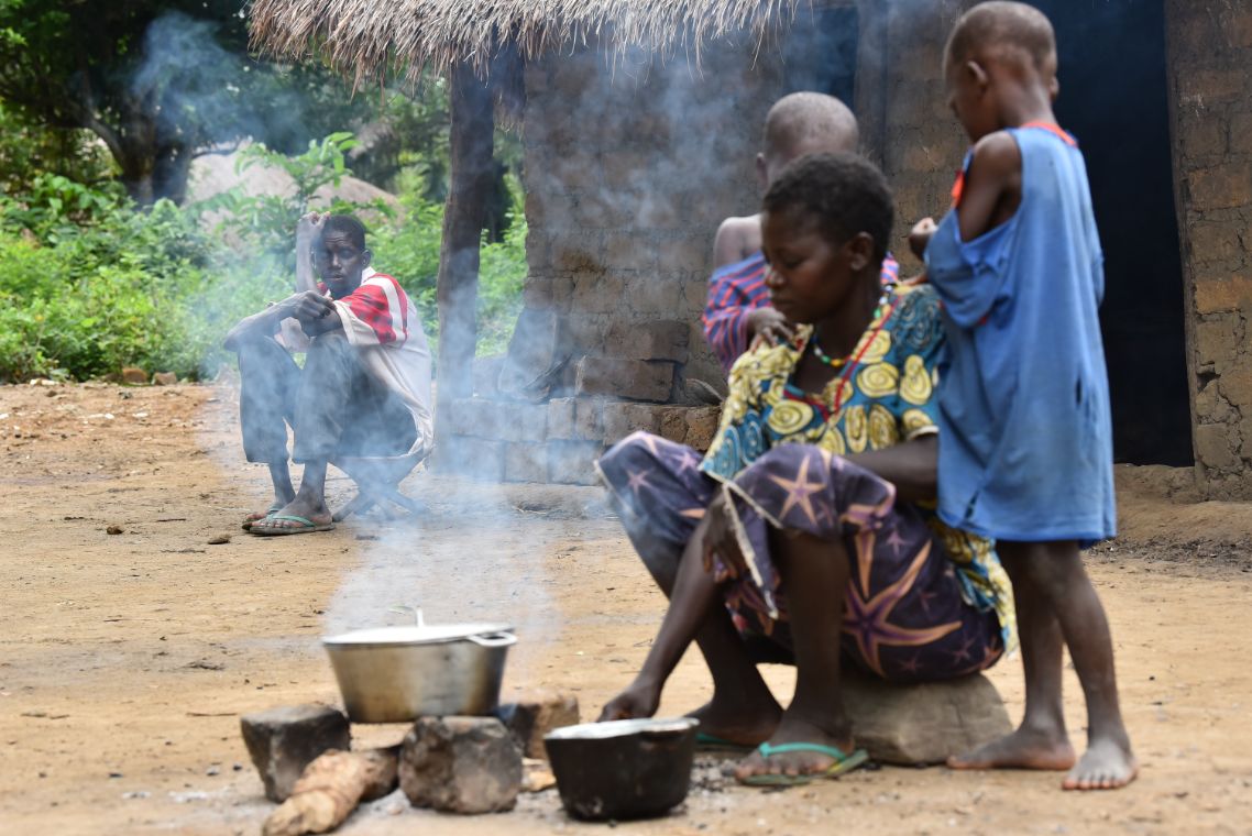 Eine Frau sitzt an einer Feuerstelle mit drei Kindern. Im Hintergrund sitzt ein Mann.