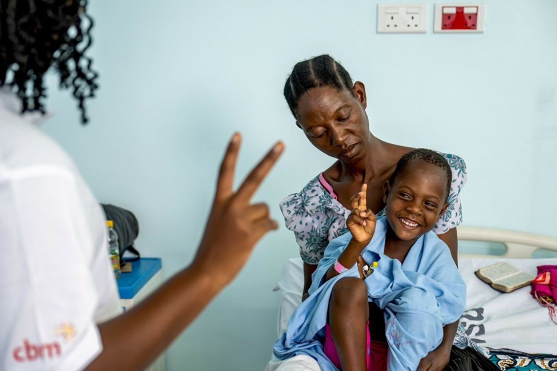 Jemand hält zwei Finger hoch und ein kleines Mädchen auf dem Schoß einer Frau macht es nach.