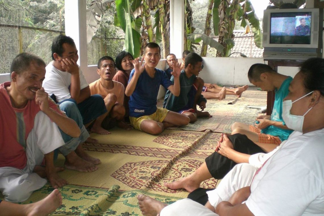 Eine Gruppe Menschen sitzt einer Hütte auf Strohmatten und diskutiert, wie man sich im Katastrophenfall nach einem Vulkanausbruch verhält.