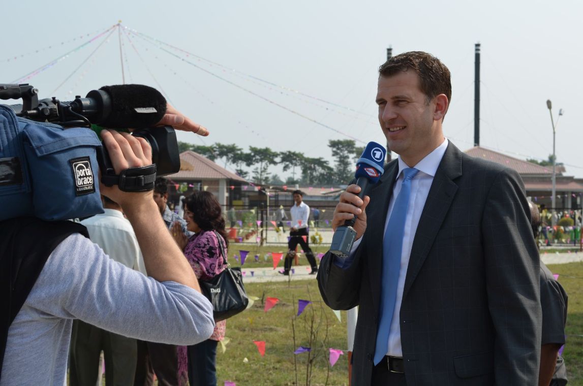 Mann mit Anzug und Mikrofon spricht vor einer Kamera