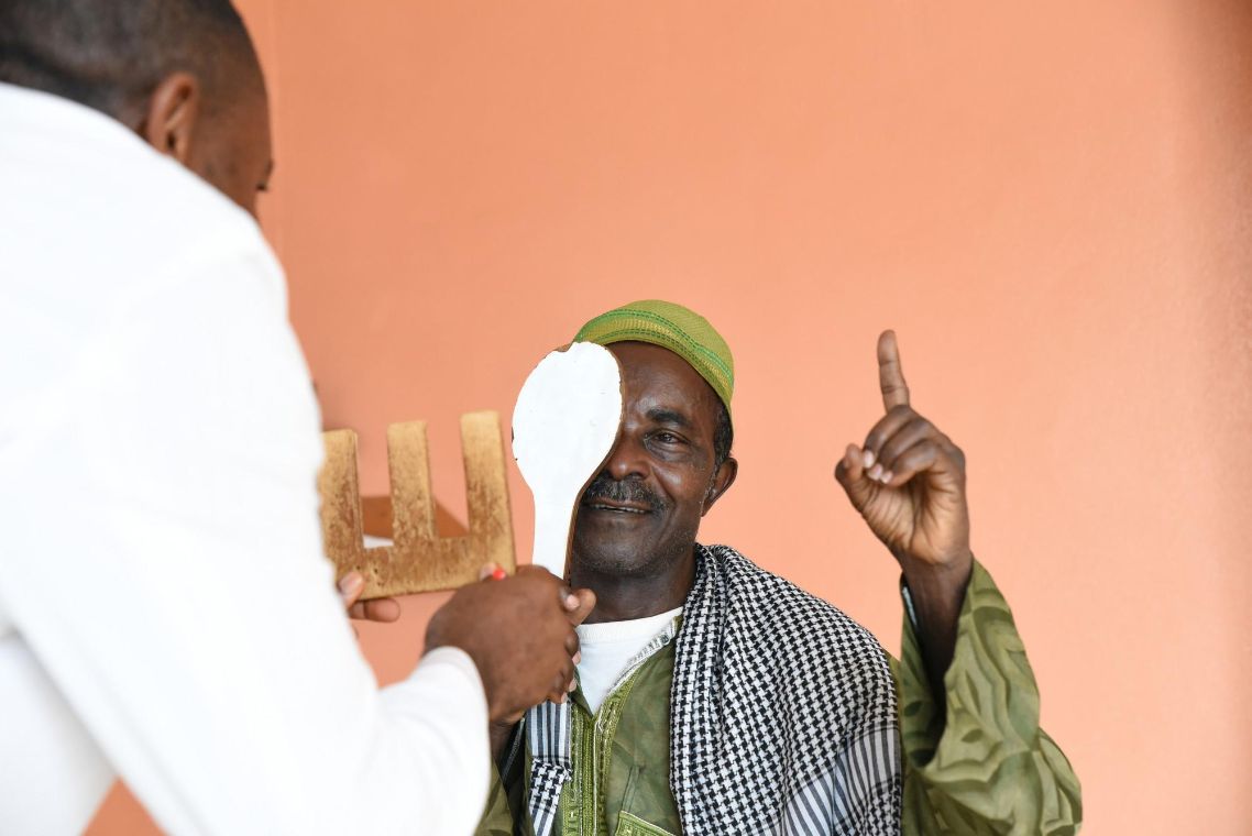 Ein Mann im weißen Kittel macht mit einer Frau einen Sehtest.