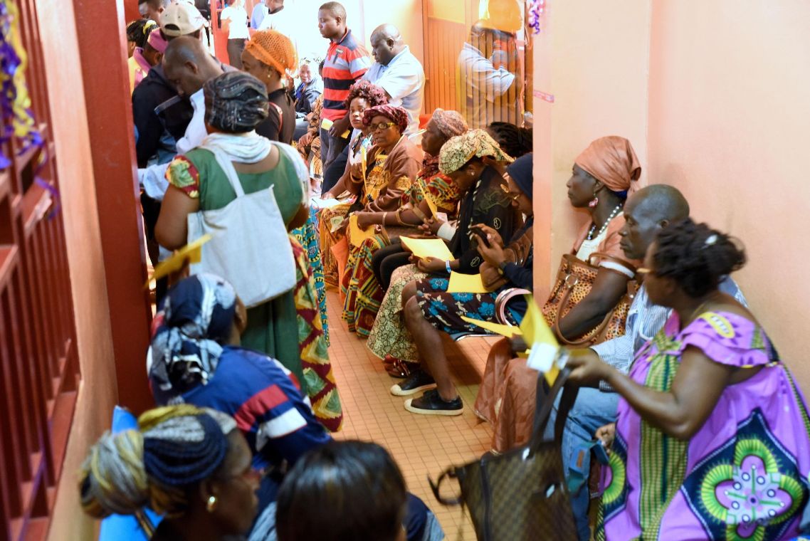 In einem Flur wartende Männer und Frauen in bunter Kleidung