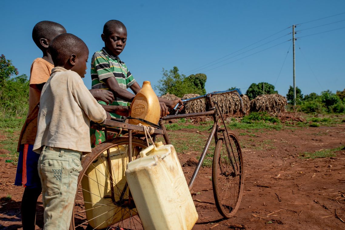 Drei kleine Jungen beladen ein Fahrrad mit Wasserkanistern aus Plastik.