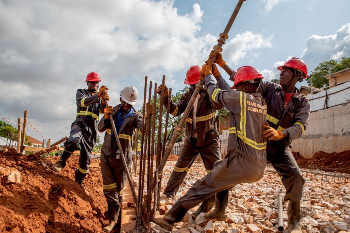 Drei Männer in Arbeitskleidung und mit Helmen biegen mit Metallrohren die Stahlstäbe für ein Gebäudefundament.