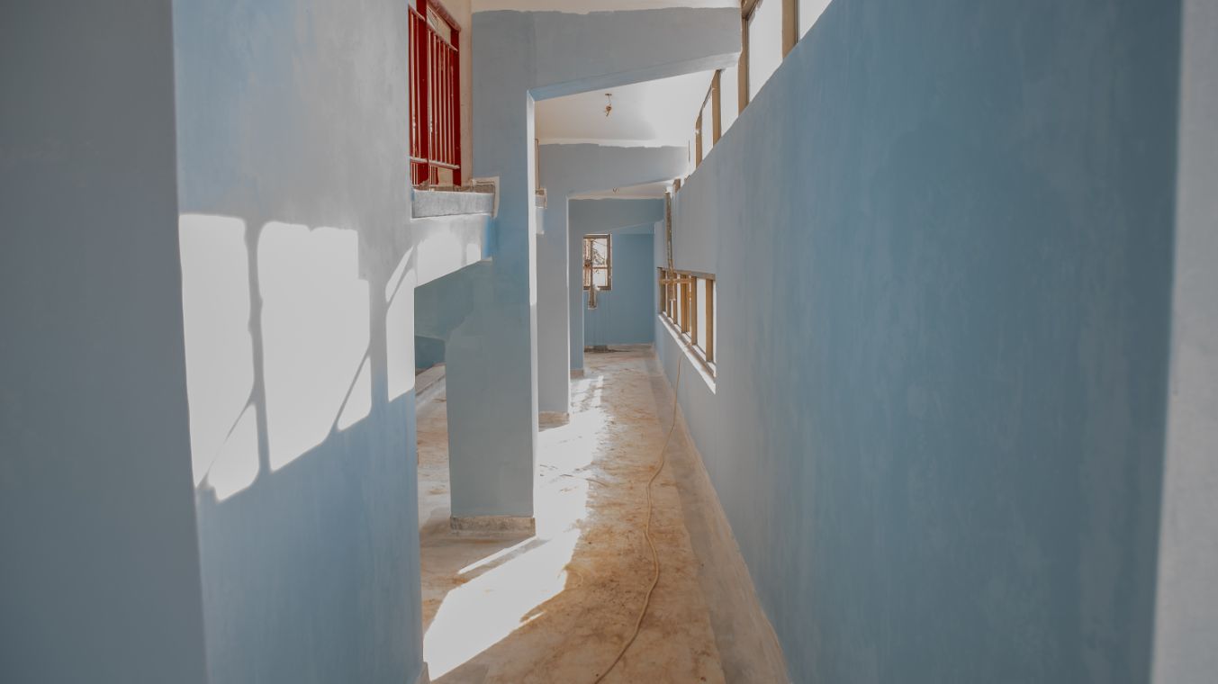 Die Sonne strahlt durch kleine Fenster auf die hellbblau gestrichene Wand eines langen Flurs.