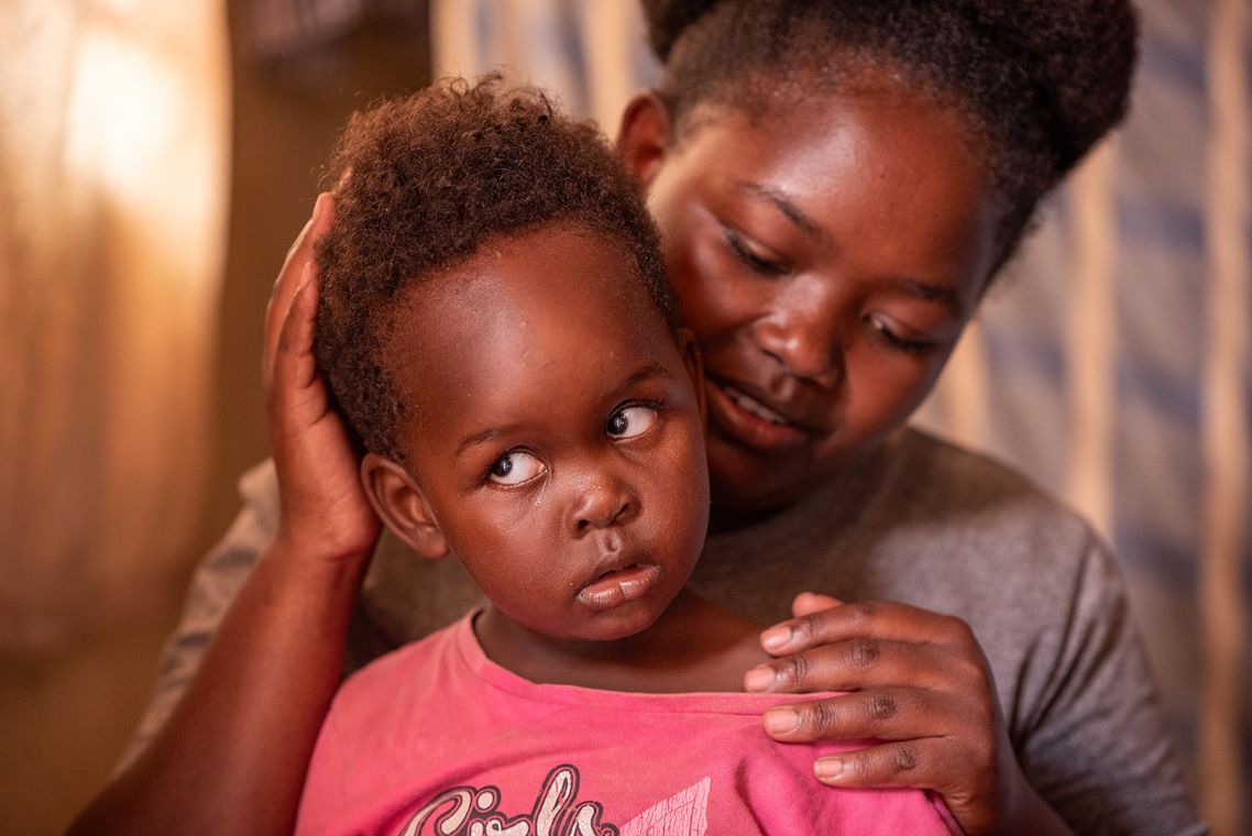 Eine Frau legt die Hände auf Kopf und Schulter eines kleinen Mädchen, das die Augen nach oben dreht und weiße Pupillen hat.