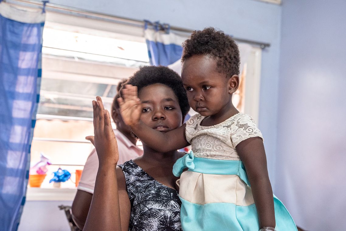 Eine Frau hält ein kleines Mädchen im Arm und hält ihm die Hand hin. Das Kind hält der Frau die Hand hin.