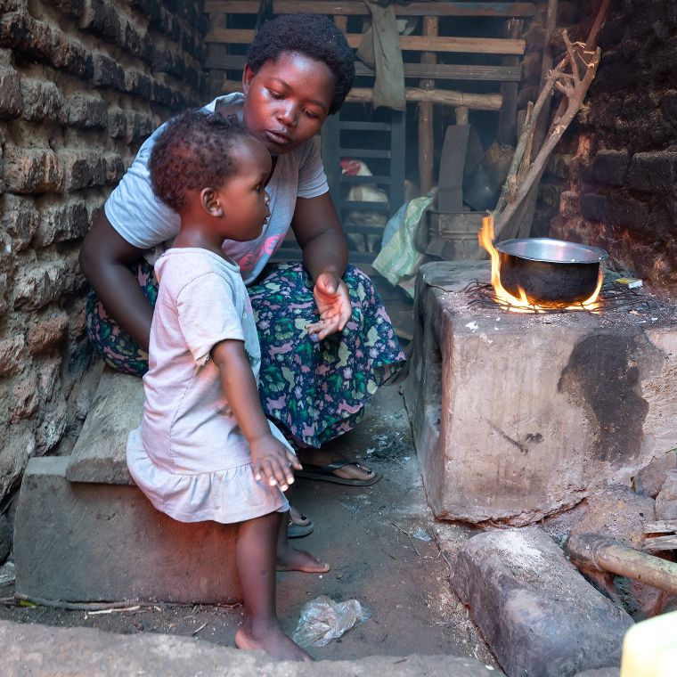 Eine Frau und ein kleines Mädchen stehen vor einem Kochfeuer.