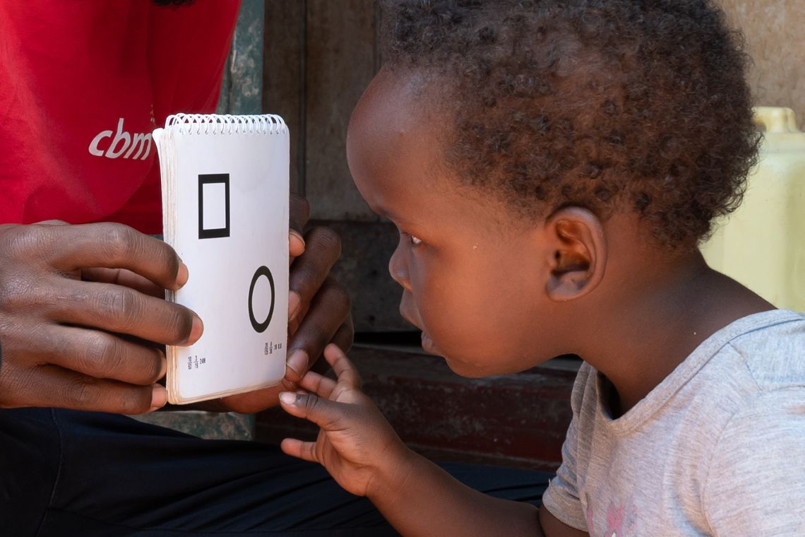 Ein kleines Mädchen beugt den Kopf vor eine Karte, auf die ein Quadrat und ein Kreis aufgedruckt ist.